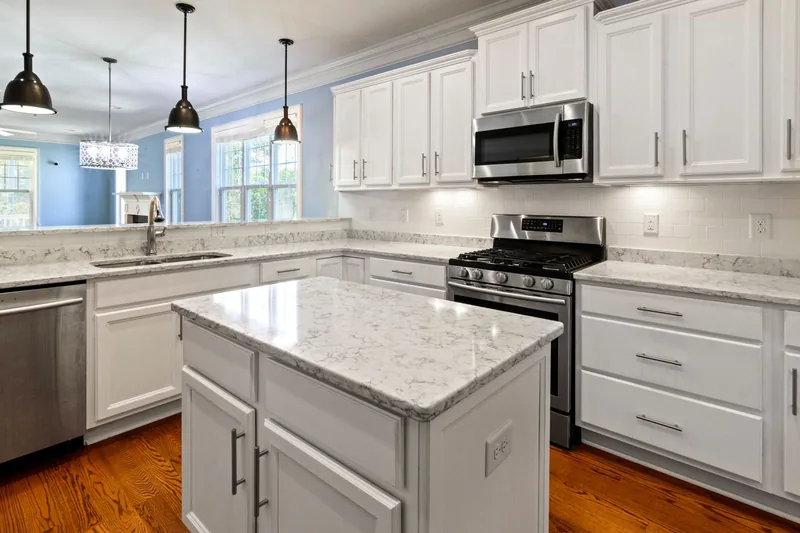 Clean white kitchen with island and marble counters in daylight